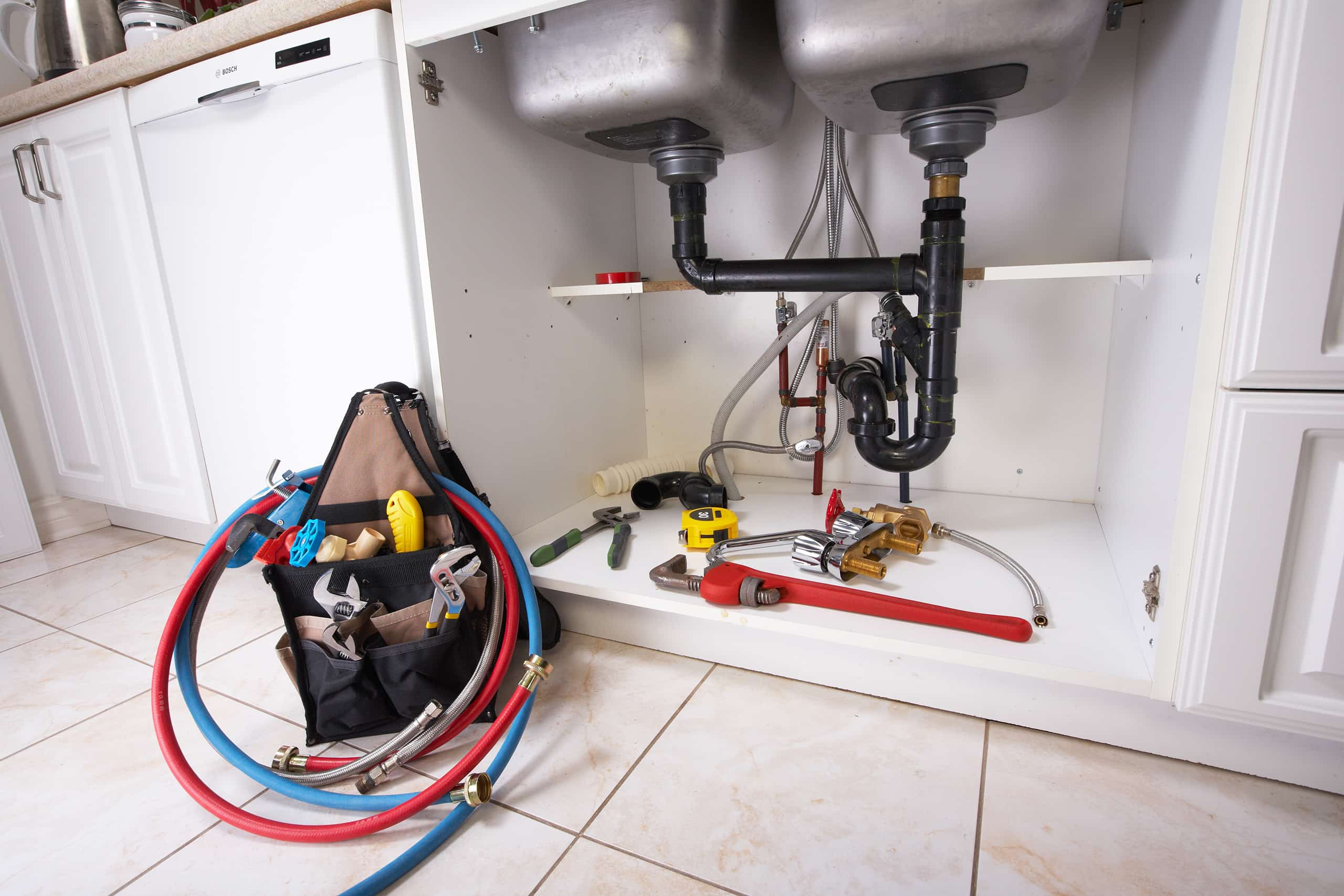 Pipes underneath of a sink with a number of tools on the floor