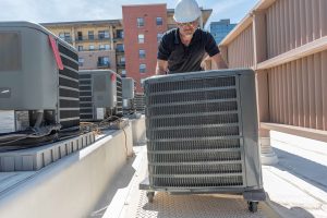 A worker moving an HVAC unit into place on the roof of a building