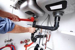 A plumber tightening pipes under a sink