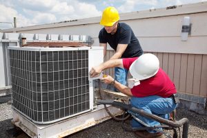 Two workers repairing an HVAC unit on the roof of a building